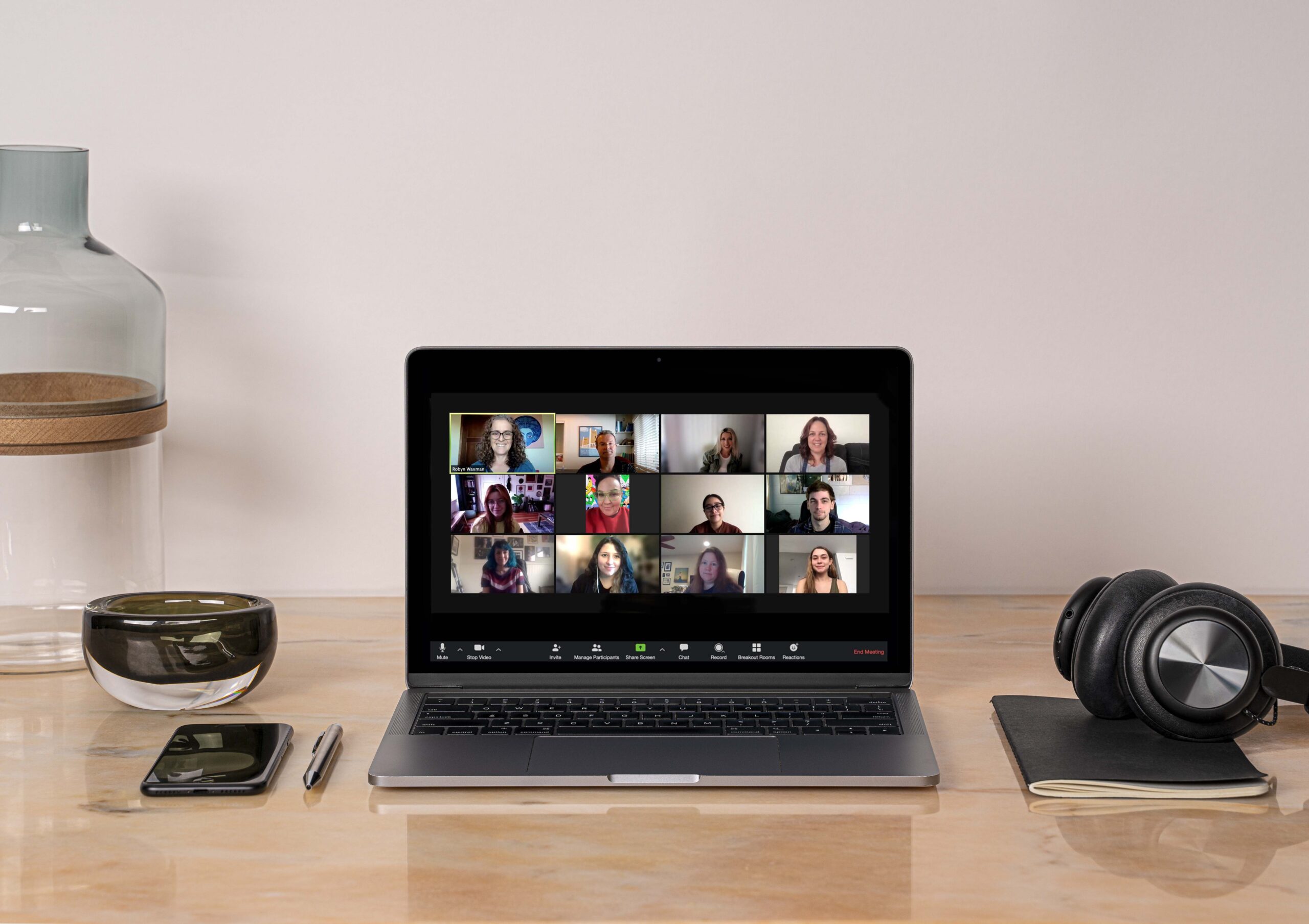 A wood top desk with an open laptop. The laptop has a Zoom meeting displayed. There are headphones and other items on the desk next to the laptop.
